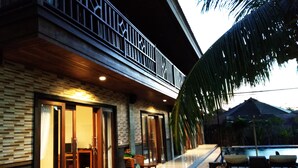 Un edificio moderno con balcón, zona de piscina con tumbonas y una palmera.