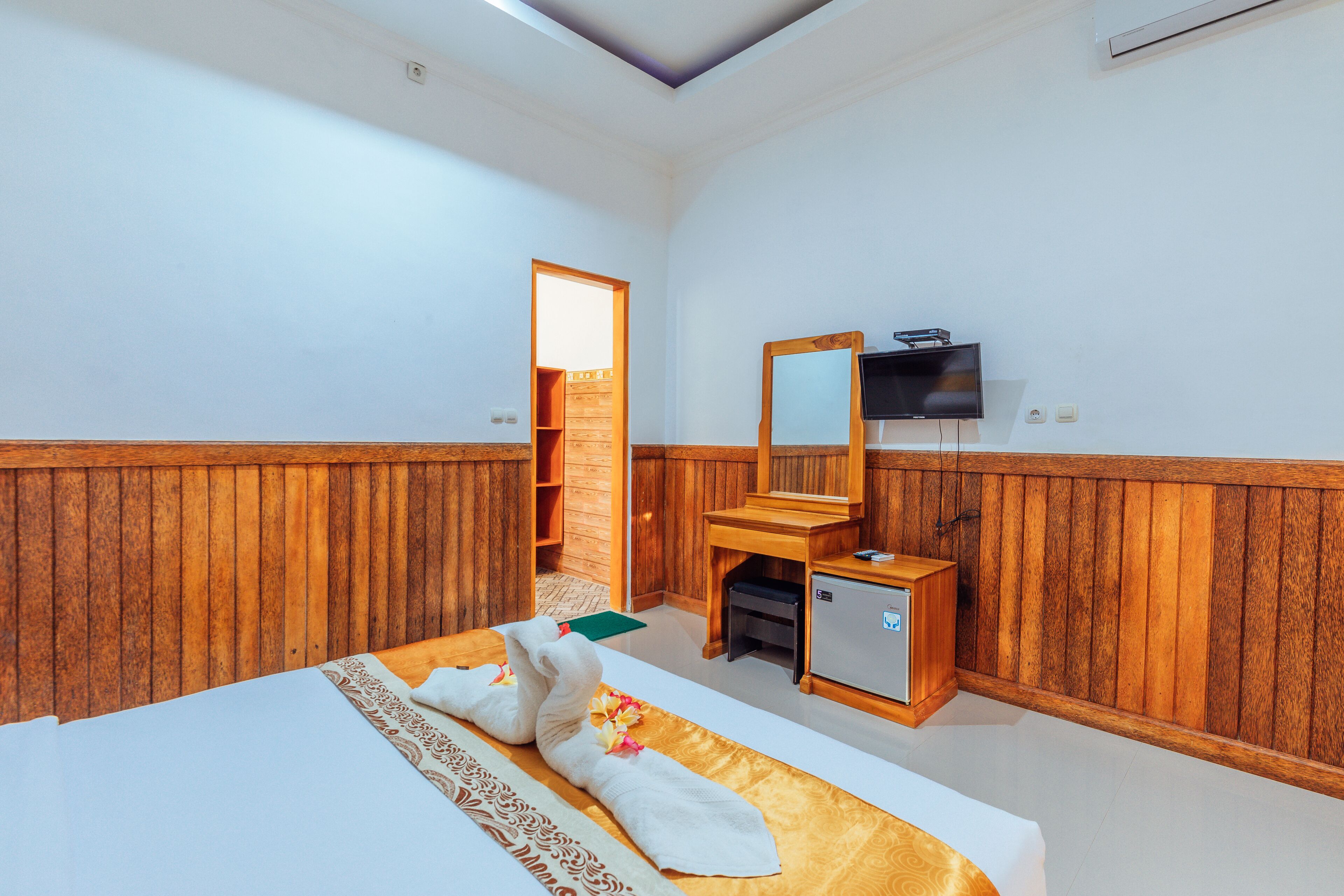 A hotel room with a wooden paneled wall, a bed with towels, a small desk, a television, and a wardrobe.