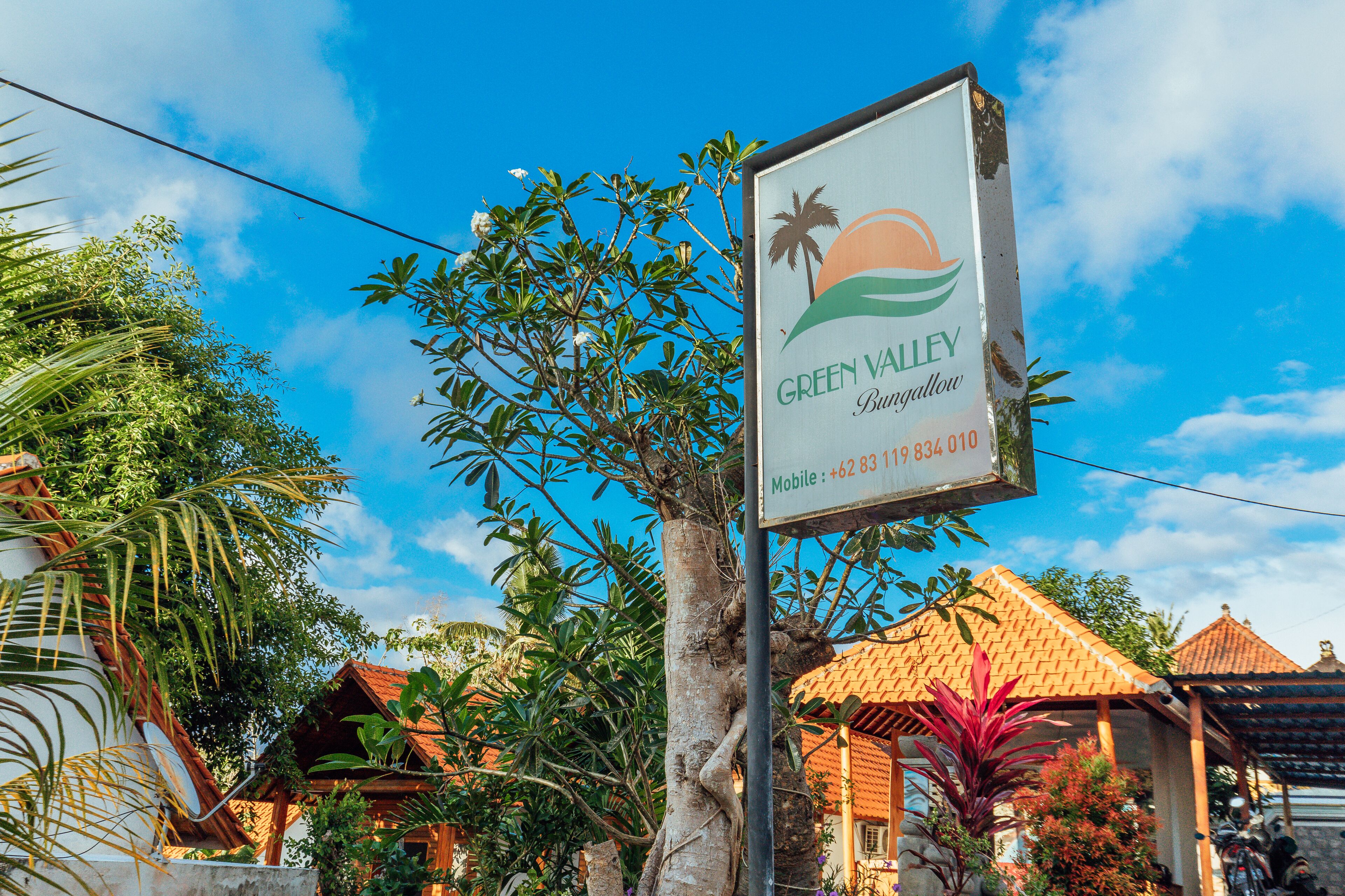 A sign for Green Valley Bungalows with a tropical theme, surrounded by lush greenery and traditional architecture.