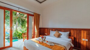 Een hotelkamer met een houten hoofdeinde, een bed met witte lakens, een groene mat en een handdoek met bloemen.