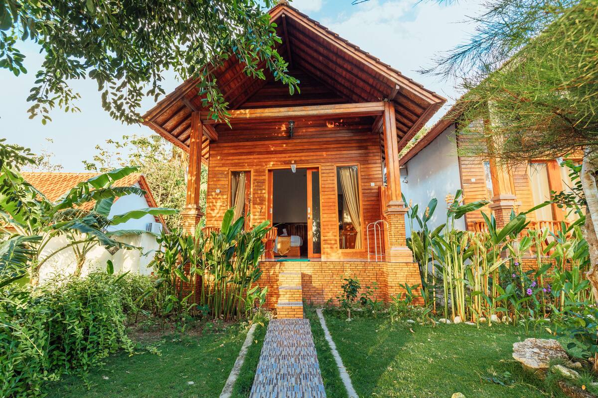 A wooden house with a brick exterior, surrounded by lush greenery and a clear sky.
