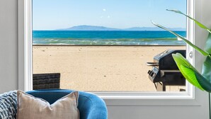 Una habitación con vistas a la playa, un sillón azul, una planta en maceta y una parrilla afuera de la ventana.