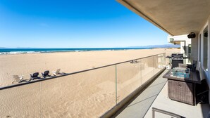 Un balcón con vista a la playa, mobiliario exterior y una parrilla.