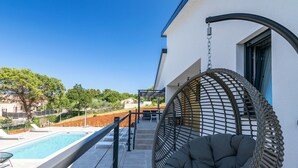 A balcony with a hanging chair, a pool, and a view of the surrounding landscape. - Villa Bellavu in Rakalj (Rakalj)