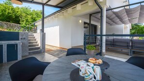 An outdoor patio with a round table, black chairs, and a covered seating area. - Villa Bellavu in Rakalj (Rakalj)