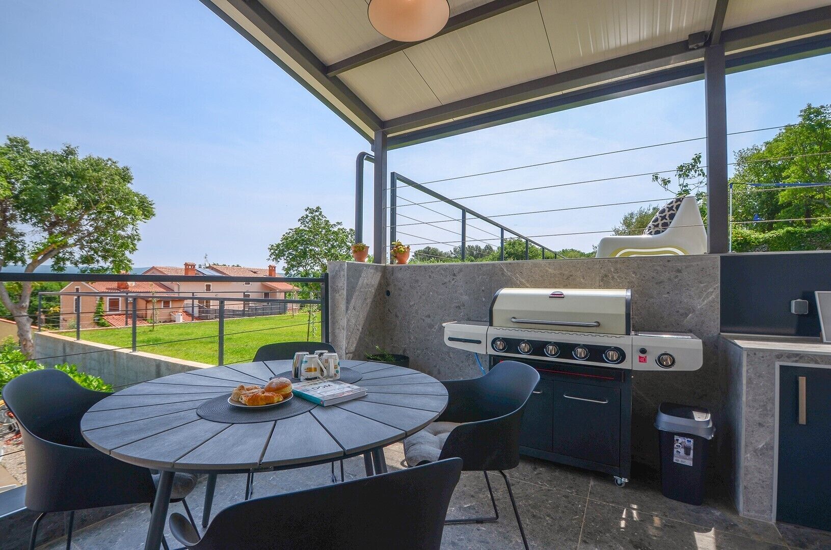 Une terrasse extérieure avec une table ronde, des chaises, un barbecue et une vue sur un quartier résidentiel.
