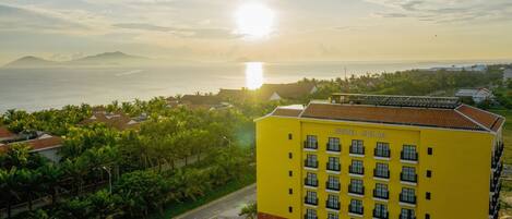 A yellow building with the name 'FIVITEL HOAN' on its facade, surrounded by lush greenery and a view of the sea.