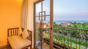 A balcony with a view of the sea and palm trees. - Fivitel Hoi An Hotel (Da Nang)