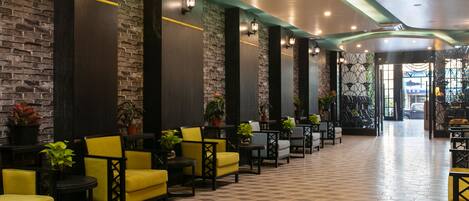 A hotel lobby with a checkered floor, yellow and black chairs, and potted plants.