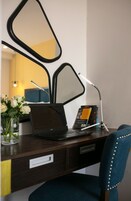 A hotel desk with a laptop, a mirror, a lamp, and a vase with flowers.