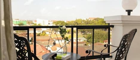 A balcony with two chairs and a table, a small potted plant, and a view of buildings and trees.