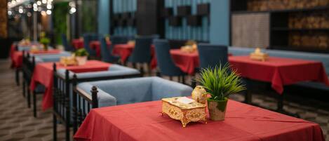 Un restaurante con mesas cubiertas de manteles rojos, sillas y objetos decorativos como una caja dorada y una planta.