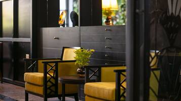 Un lobby moderno con una decoración en tonos negro y amarillo, que incluye una zona de estar con sillas amarillas y una pequeña mesa, además de un espejo grande que refleja el interior.