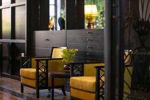 Un lobby moderno con una decoración en tonos negro y amarillo, que incluye una zona de estar con sillas amarillas y una pequeña mesa, además de un espejo grande que refleja el interior.