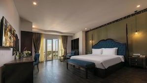 A spacious bedroom with a large bed, a desk, and a chair. There is a large window with curtains and a view of the outdoors. - Azalea Parkview Hotel (Vientiane)