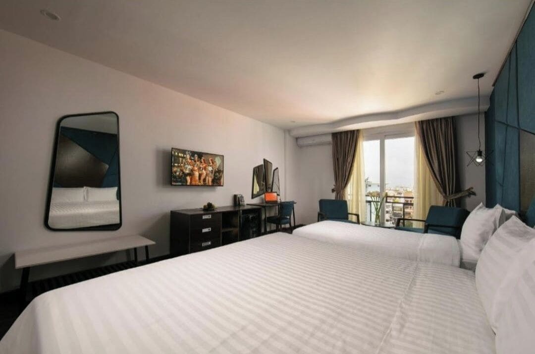 Habitación de hotel con una cama grande, un escritorio, una silla, un televisor y vistas a la ciudad.