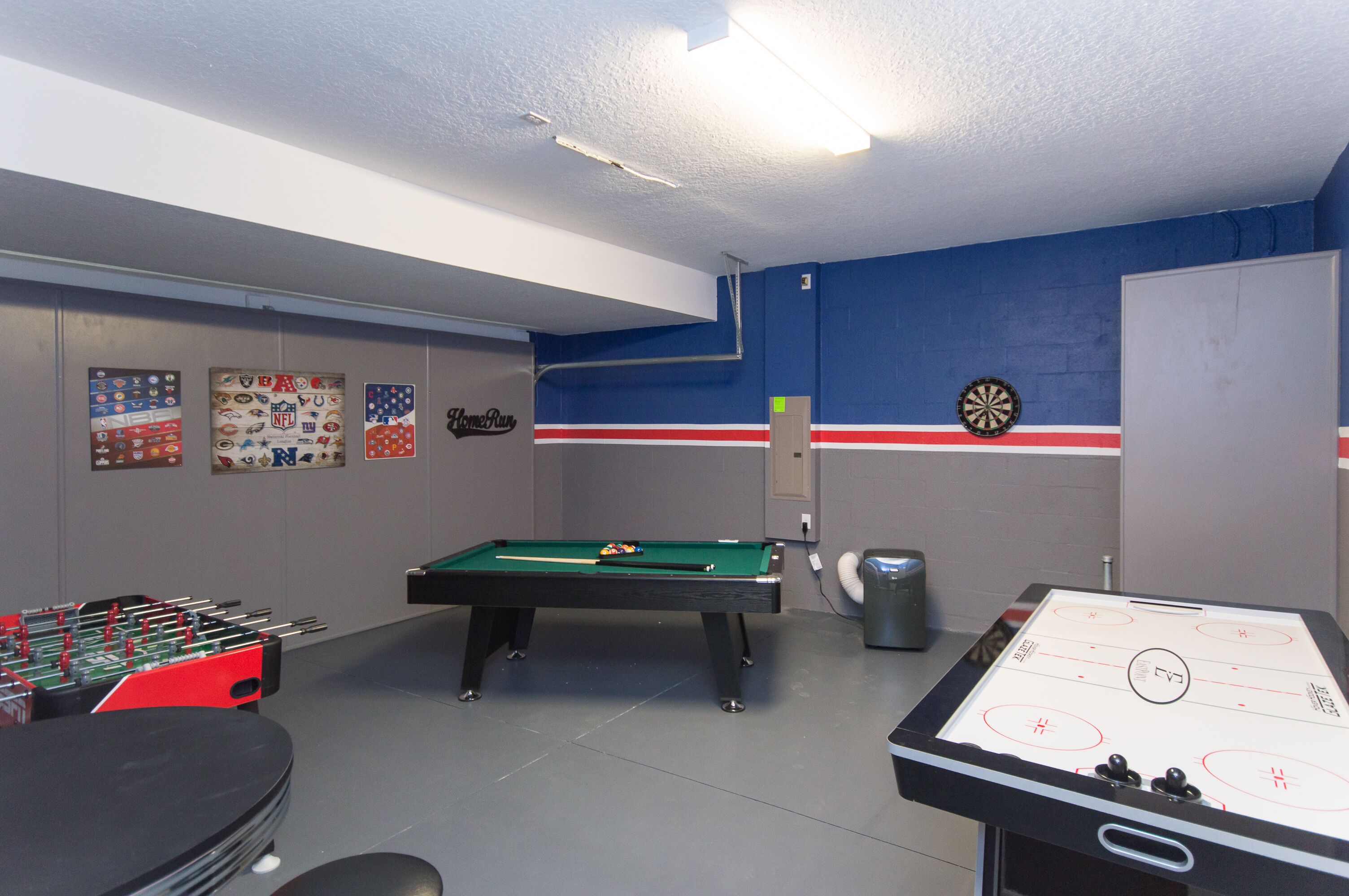A room with a pool table, foosball table, dartboard, and various sports memorabilia on the walls.