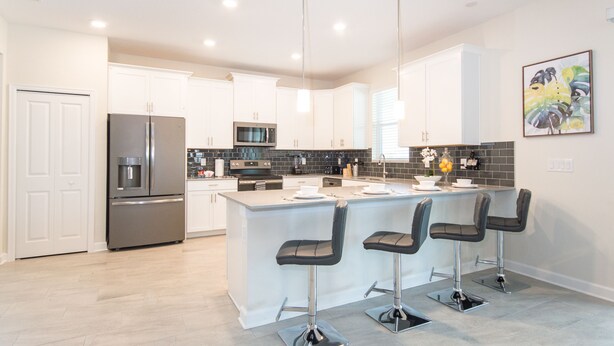 A modern kitchen with white cabinets, a stainless steel refrigerator, a microwave, and a black tiled backsplash. There are three bar stools and a small island with a sink. - 5🌟Clean Rated-Movie/Game Room, 3780 SF,❤️12p Dining (Davenport)