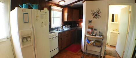 A compact kitchen with wooden flooring, a refrigerator, a stove, and a sink.
