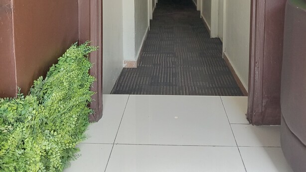 A long, narrow hallway with a tiled floor, white walls, and brown trim.