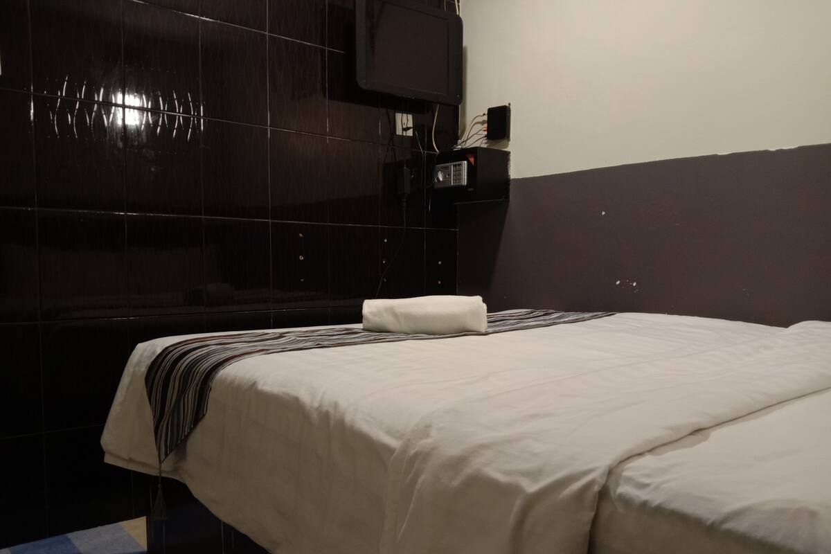 Une chambre d’hôtel avec un grand lit, un téléviseur à écran plat fixé au mur et une tête de lit de couleur sombre.