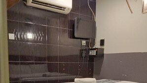 A hotel room with a bed, a TV mounted on the wall, and an air conditioning unit.