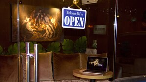A hotel lobby with a 'Welcome We're OPEN' sign, a laptop on a small table, and green upholstered seating.