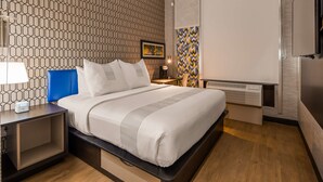 Moderni hotellihuone, jossa on siististi pedattu sänky, yöpöytä lampun kanssa, työpöytä ja tuoli.