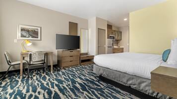 A hotel room with a bed, a desk with a chair, a television, a microwave, and a small kitchenette.