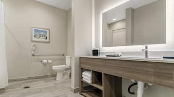 Une salle de bain moderne avec un meuble-lavabo en bois, un grand miroir et des toilettes équipées d’une barre d’appui.