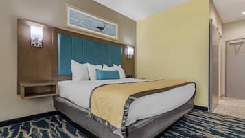 A hotel room with a large bed, a headboard with a teal panel, a small bedside table, a wall-mounted light, and a framed picture above the bed.