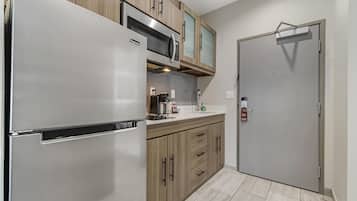A modern kitchen with a stainless steel refrigerator, wooden cabinets, a microwave, and a coffee maker.
