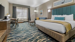 Una habitación de hotel con cama, escritorio, silla y un ventanal con cortinas.
