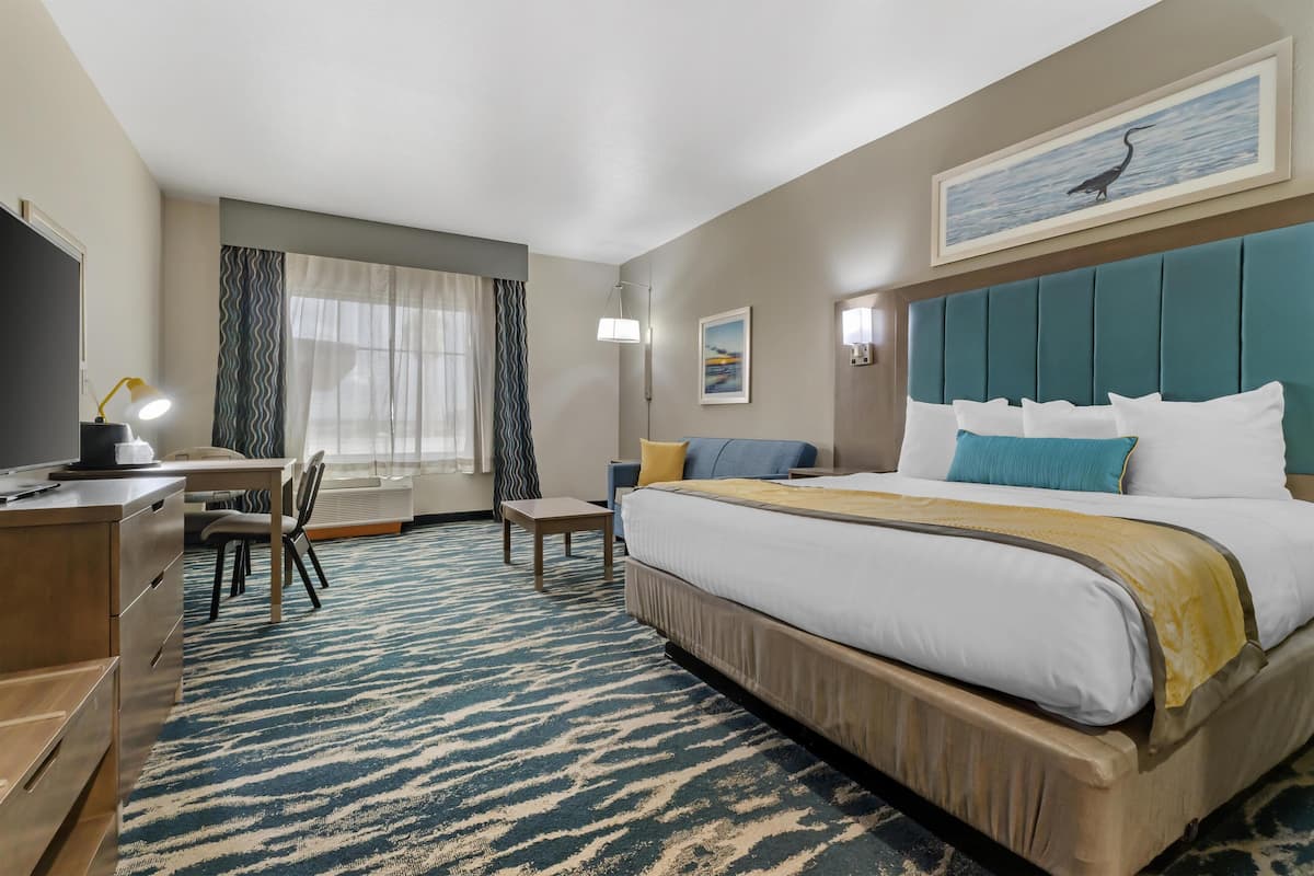 Una habitación de hotel con cama, escritorio, silla y un ventanal con cortinas.