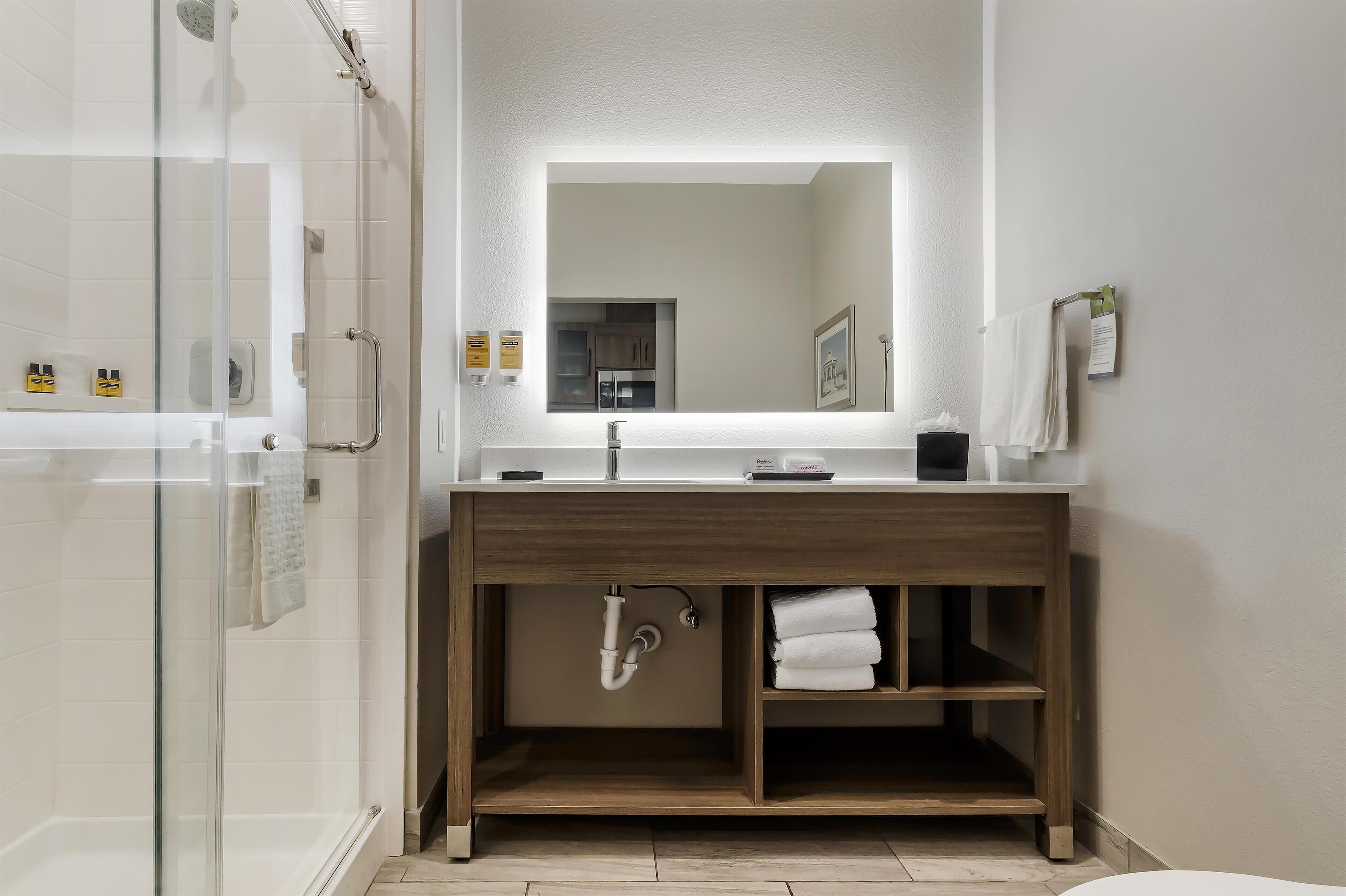 A modern bathroom with a glass shower enclosure, a wooden vanity with a mirror, and a towel rack.