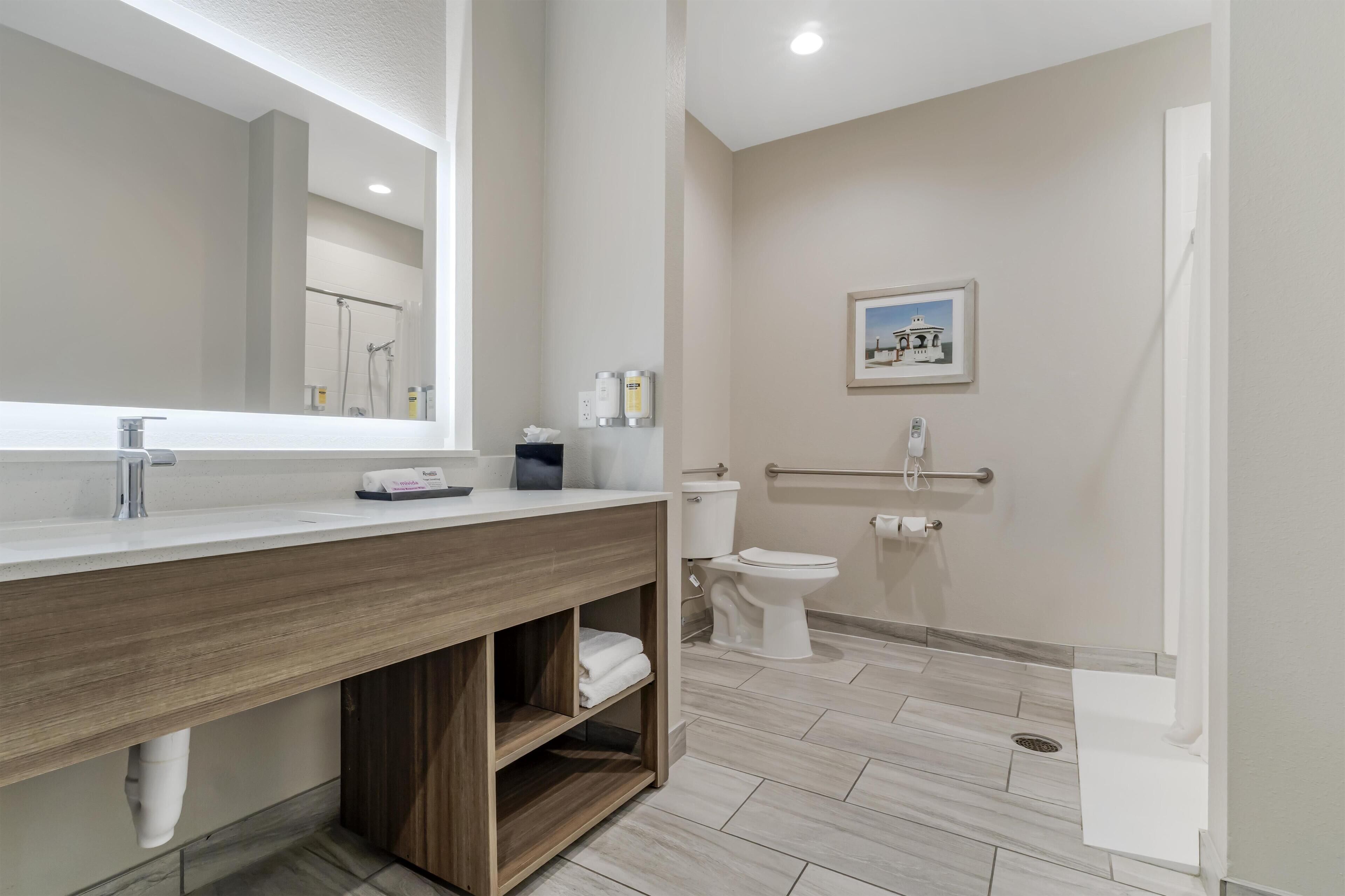 Un baño moderno con tocador de madera, un espejo grande, un inodoro y una zona de ducha.