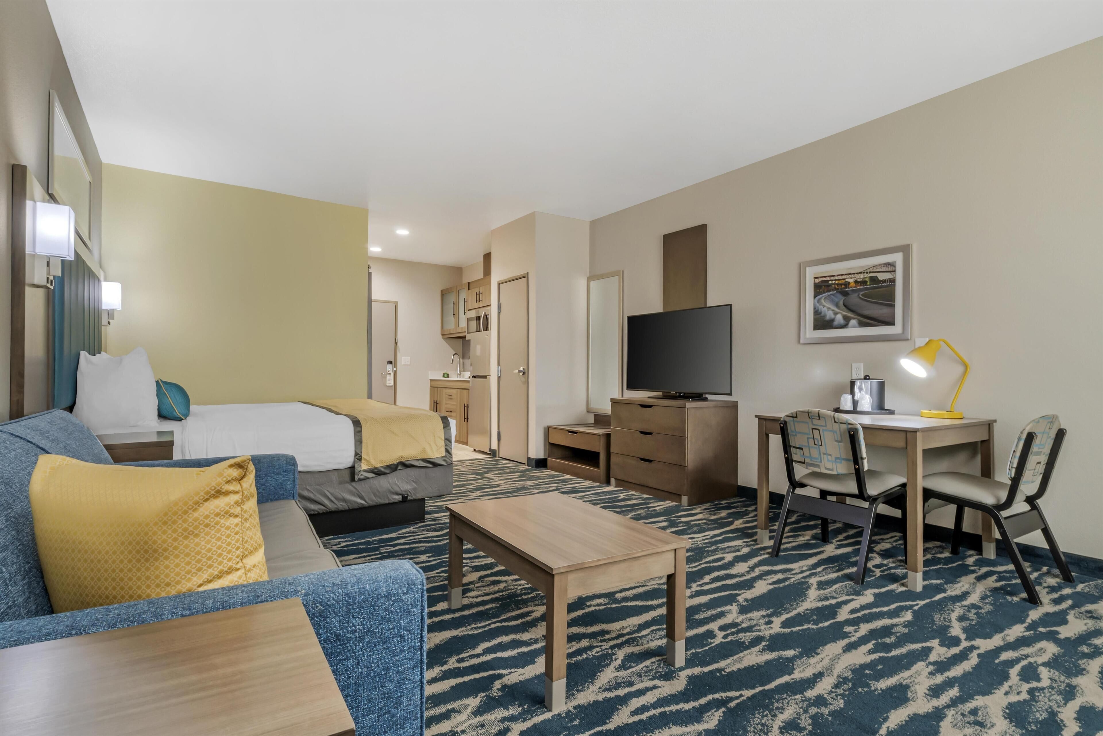 A hotel room with a bed, sofa, TV, desk, and a small kitchenette.