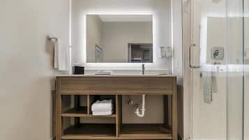 A modern bathroom with a wooden vanity, a large mirror, a glass shower enclosure, and a towel rack.