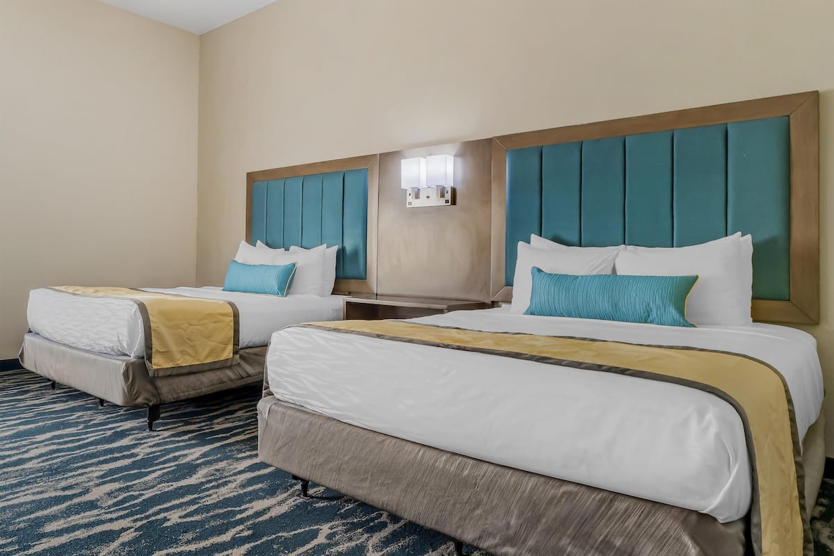 Una habitación de hotel con dos camas, cada una con cabecero, mesita de noche y lámpara.