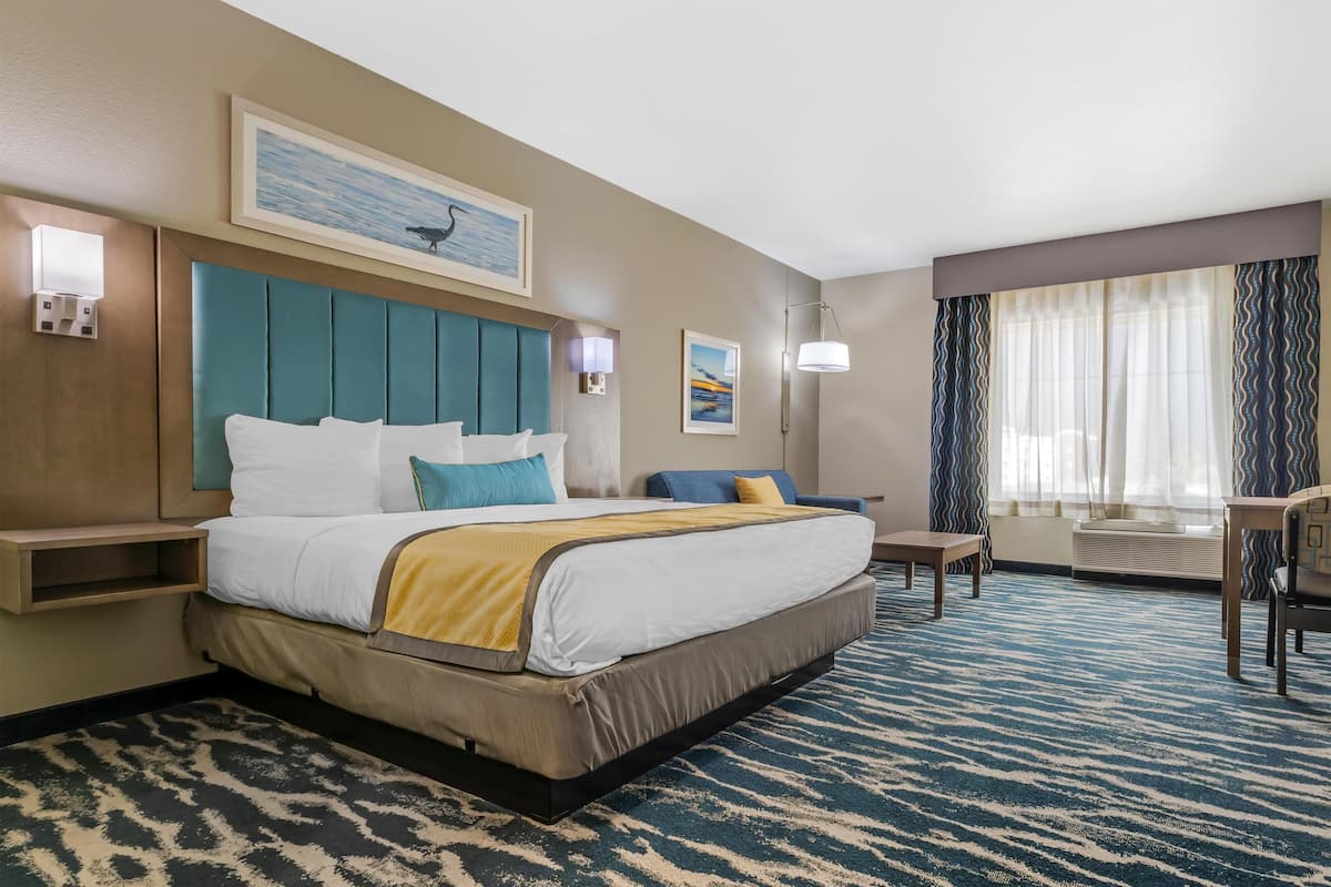 Habitación de hotel con una cama grande, un escritorio, una silla, una ventana con cortinas y obras de arte en las paredes.