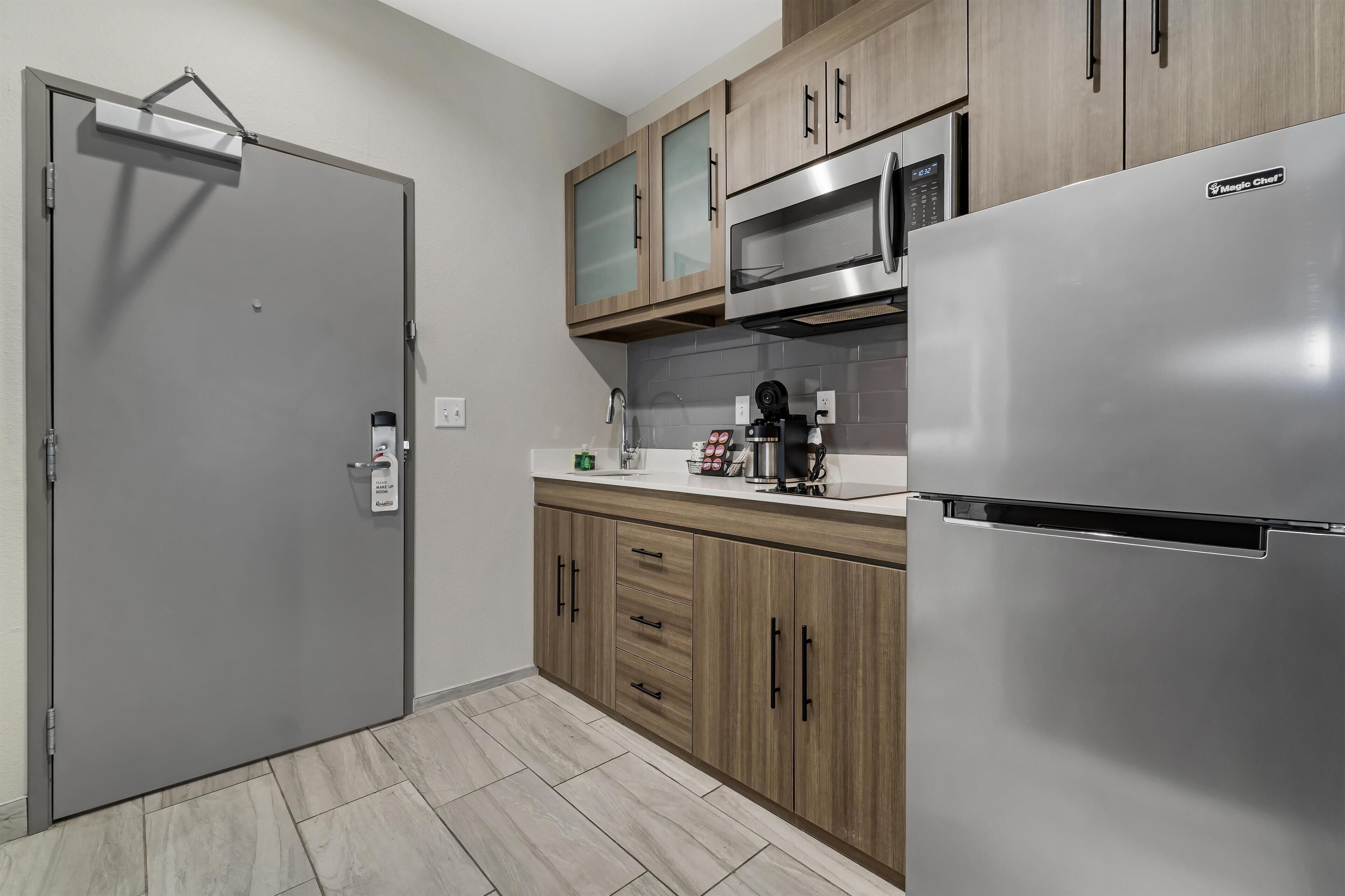 A modern kitchen with a stainless steel refrigerator, wooden cabinets, a microwave, and a built-in oven.