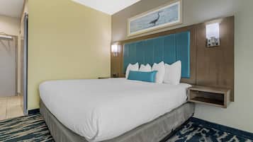 Habitación de hotel con una cama grande, cabecera con panel color turquesa, un cuadro enmarcado sobre la cama y una mesita de noche con una lámpara.