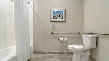 A bathroom with a white bathtub, a toilet, and a framed picture on the wall.