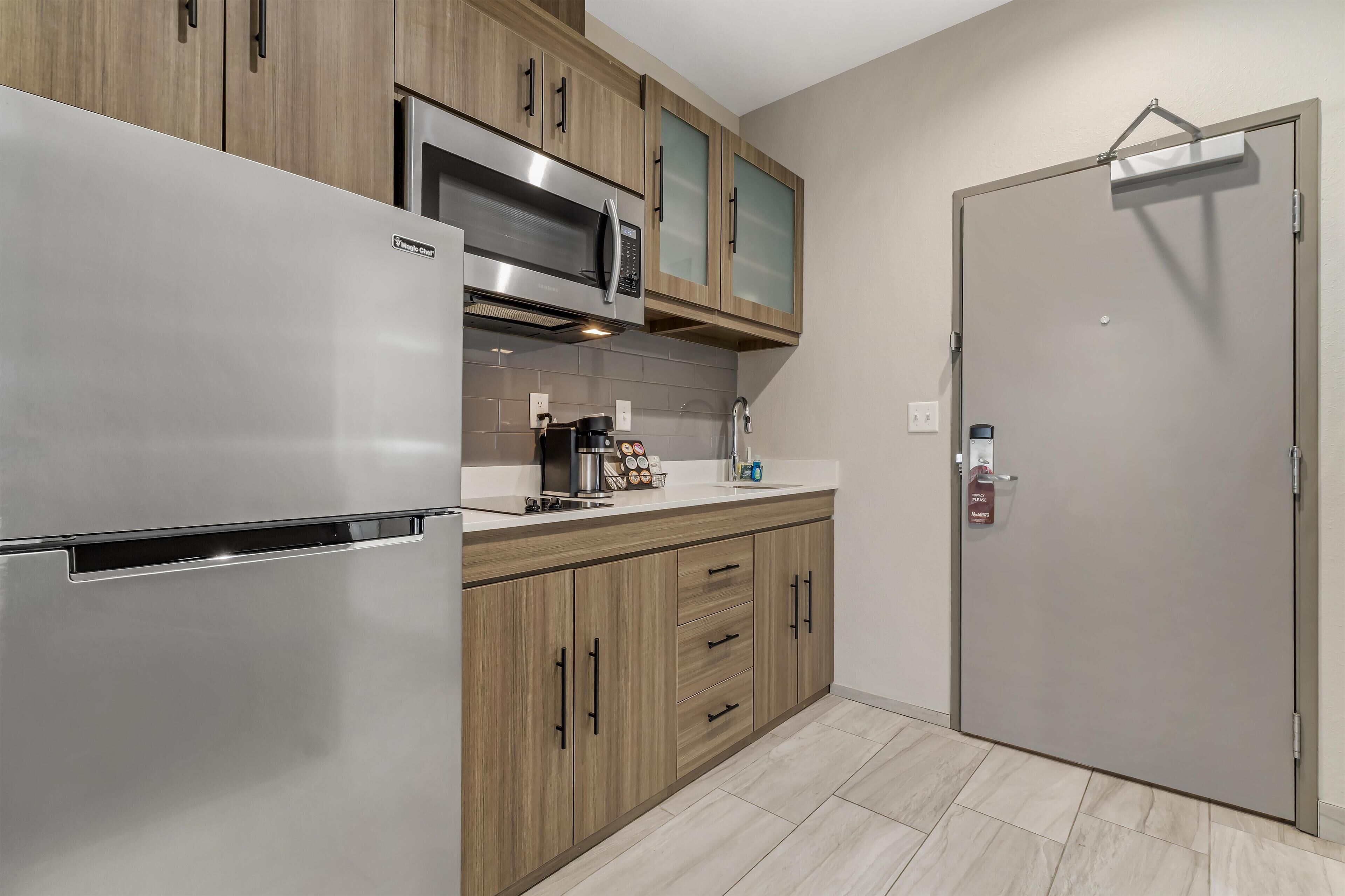 Una cocina moderna con un refrigerador de acero inoxidable, armarios de madera, un microondas y una cafetera.