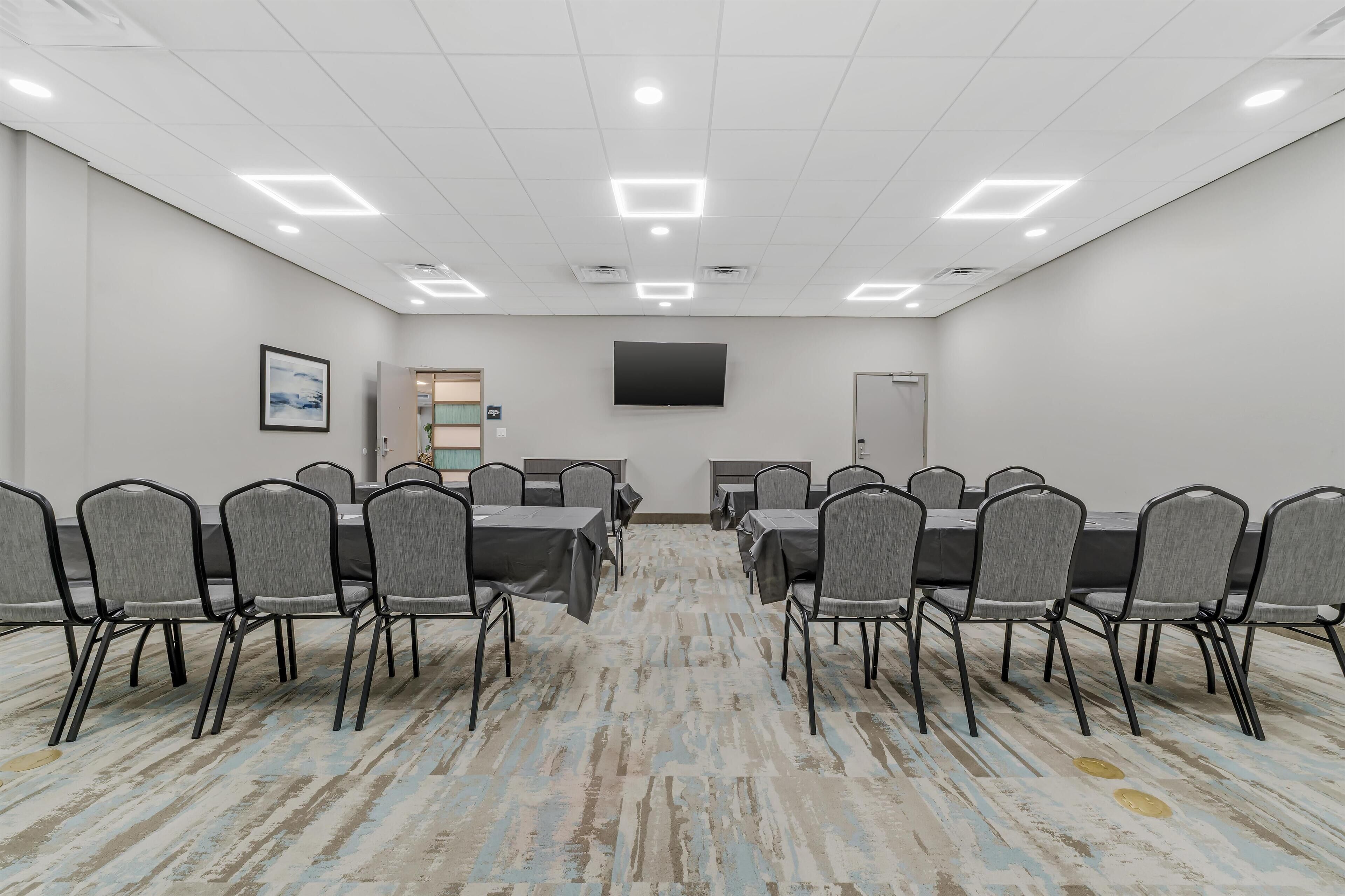 Un salón de conferencias con una larga mesa y sillas, un televisor de pantalla plana y una puerta.