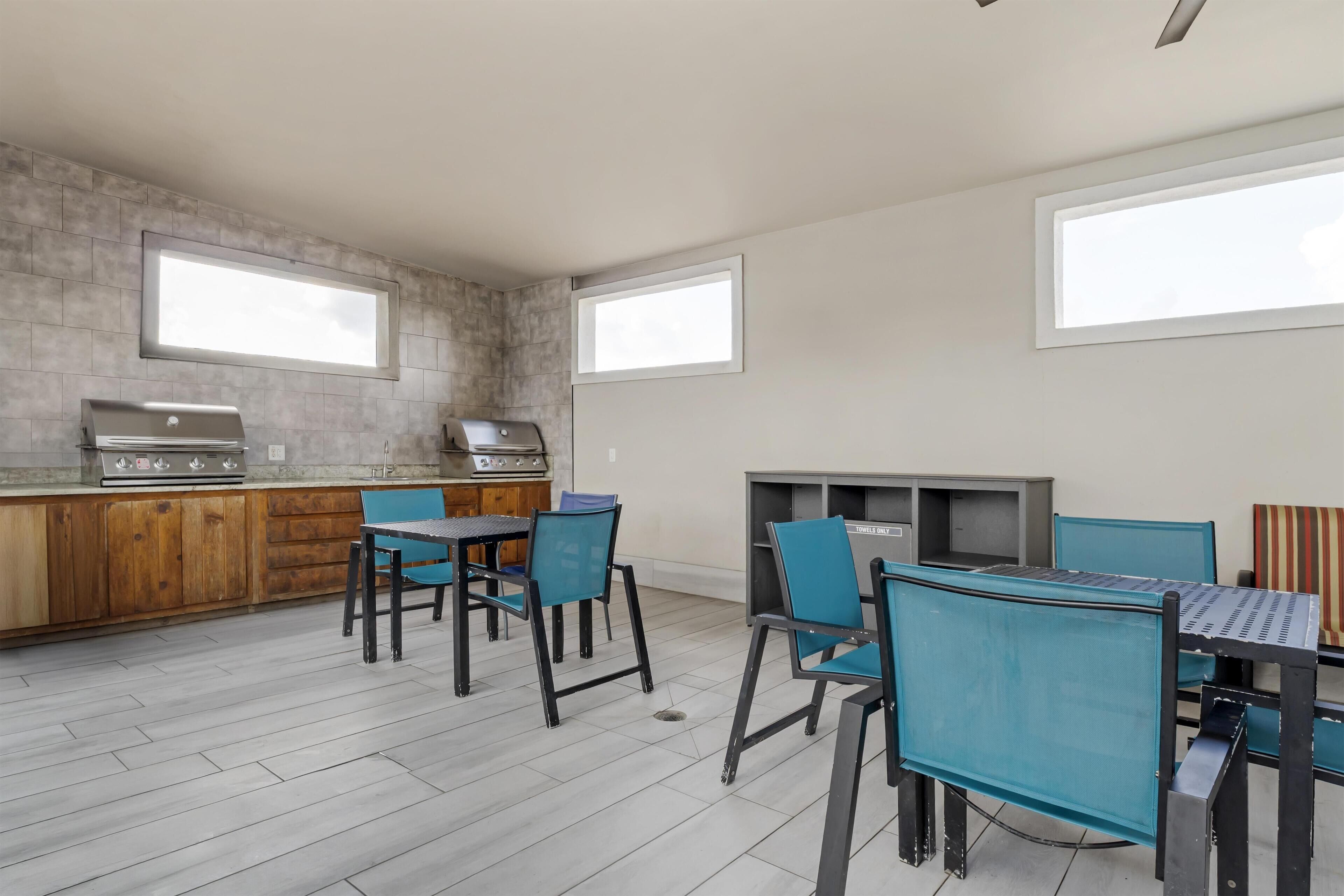 Une cuisine moderne dotée d’un barbecue intégré, de meubles en bois et d’un coin repas avec des chaises bleues et une table.