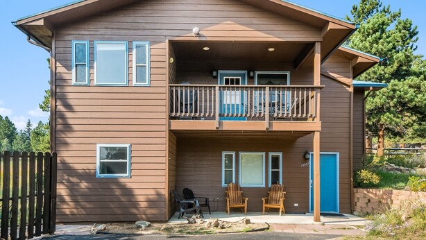 A two-story building with a balcony, a blue door, and two chairs outside.