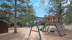 A playground with a wooden climbing structure, swings, and a tire swing.
