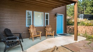 A house with a covered porch, two wooden chairs, a black chair, and a blue door.