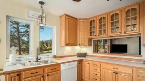 A modern kitchen with wooden cabinets, a dishwasher, and a large window offering a view of trees.